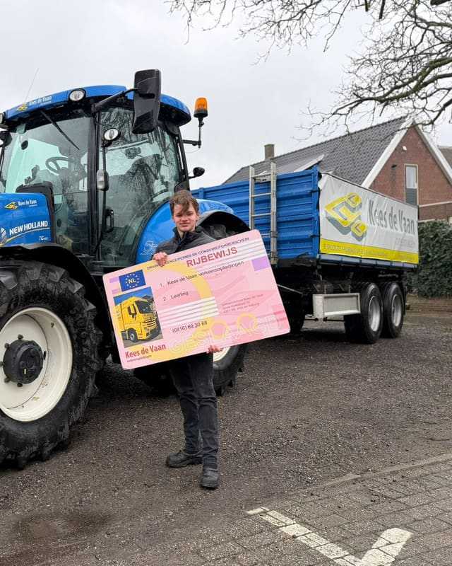 Geslaagde cursist met rijbewijsbord voor een blauwe lestrekker met aanhangwagen