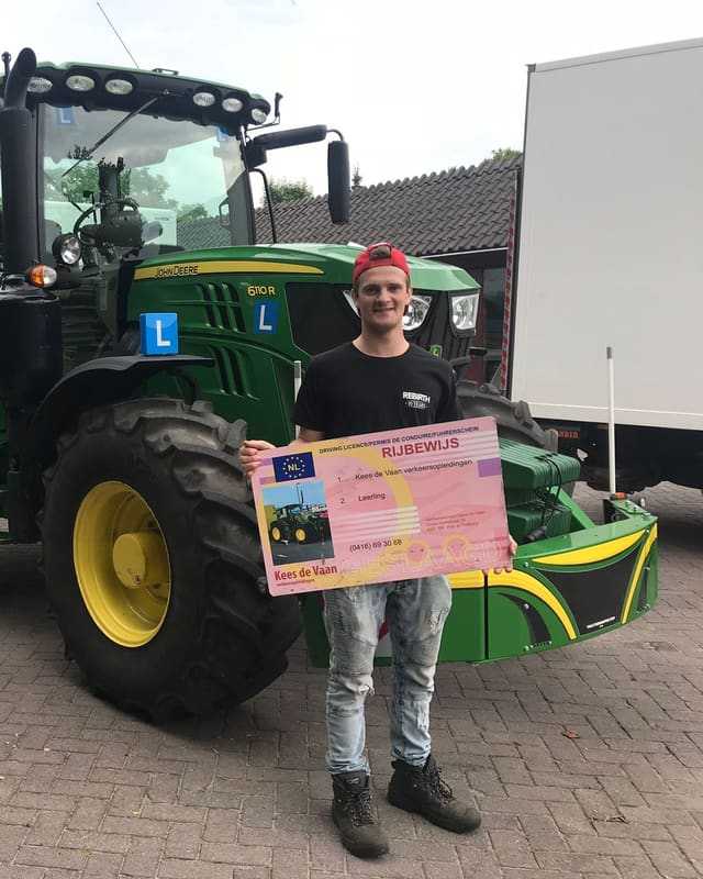 Geslaagd voor het trekkerrijbewijs: cursist met rijbewijsbord voor een groene lestrekker naast een witte oplegger