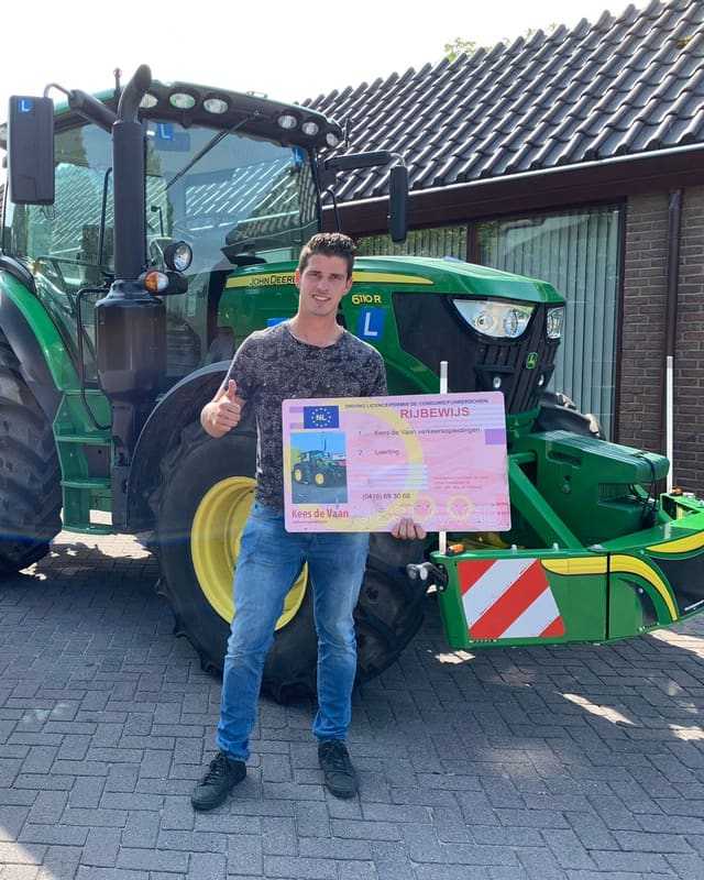 Geslaagd voor het trekkerrijbewijs: cursist steekt duim op met rijbewijsbord voor een groene lestrekker