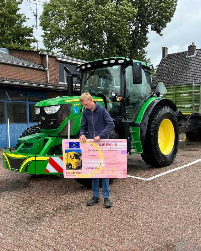 Geslaagd voor het trekkerrijbewijs: cursist in blauwe hoodie met rijbewijsbord voor een groene lestrekker