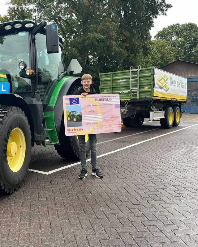Geslaagd voor het T-rijbewijs: cursist met rijbewijsbord naast een groene lestrekker met lange kipper