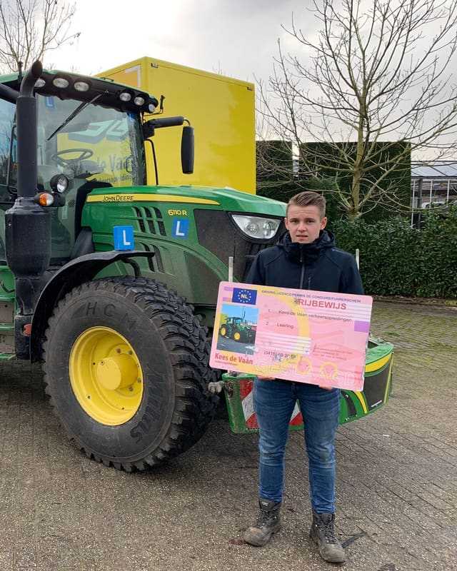 Geslaagd voor het T-rijbewijs: cursist met rijbewijsbord voor een groene lestrekker op een grijze dag