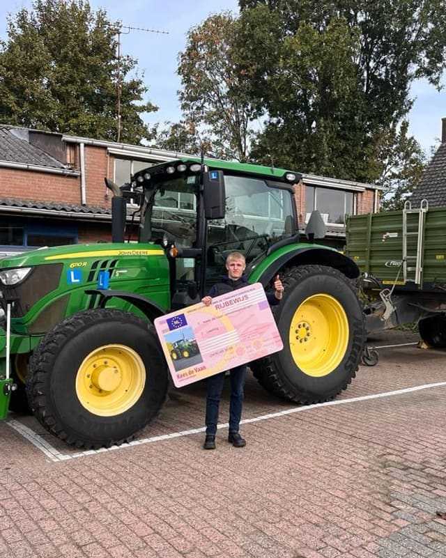 Geslaagd voor het trekkerrijbewijs: cursist houdt het rijbewijsbord schuin naast een groene lestrekker