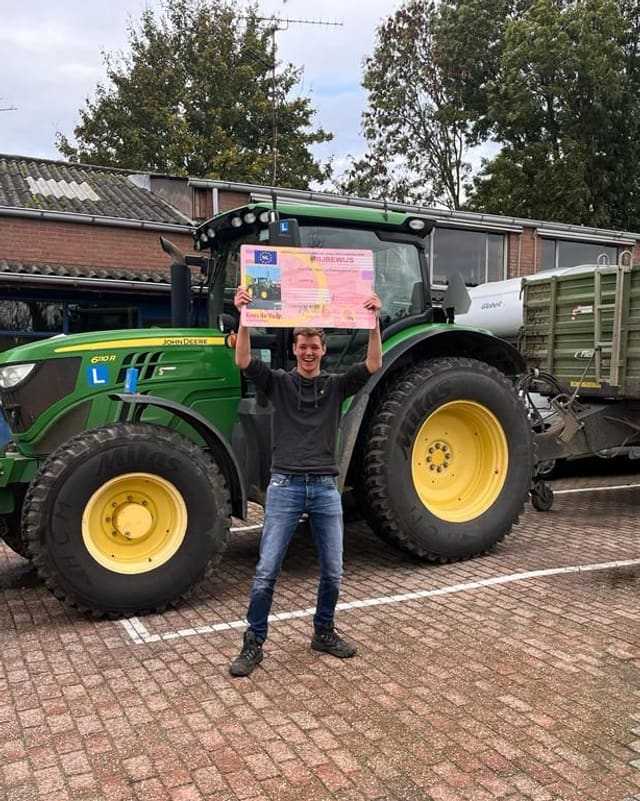 Geslaagde cursist houdt het rijbewijsbord hoog boven het hoofd voor een groene lestrekker