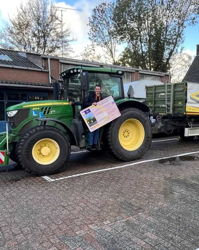 Geslaagd voor het trekkerrijbewijs: cursist met rijbewijsbord op de opstap van een groene lestrekker
