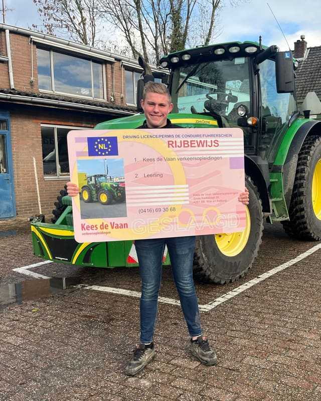 Geslaagd voor het T-rijbewijs: cursist toont trots het grote rijbewijsbord voor de lestrekker