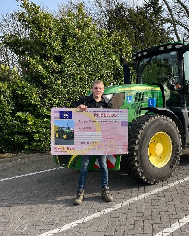 Geslaagde cursist met rijbewijsbord voor een groene lestrekker en een hoge heg