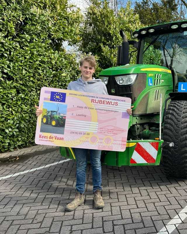 Geslaagd voor het trekkerrijbewijs: cursist met groot rijbewijsbord voor een groene lestrekker tussen het groen