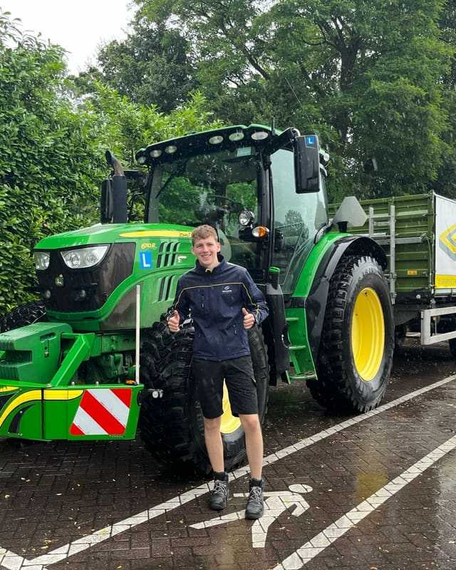 Geslaagd voor het T-rijbewijs: cursist in korte broek naast een groene lestrekker op natte klinkers