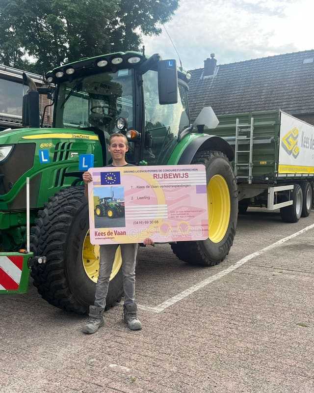 Geslaagde cursist met rijbewijsbord voor een groene lestrekker met de kipper erachter