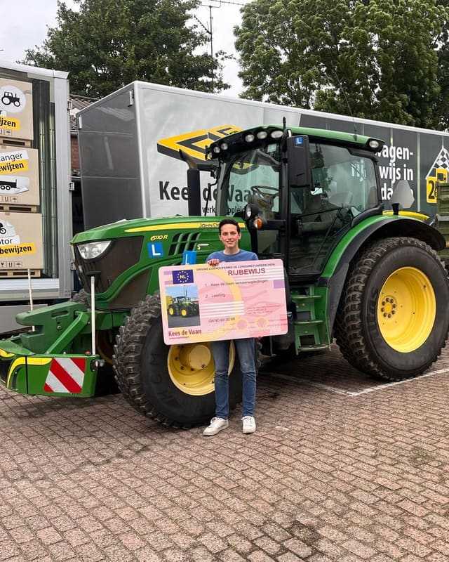 Geslaagd voor het trekkerrijbewijs: cursist met rijbewijsbord bij de lestrekker en lesvrachtwagens