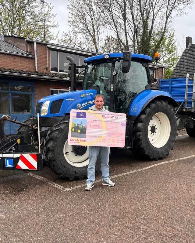 Geslaagde cursist met het rijbewijsbord voor de blauwe lestrekker en kipper op het lesterrein