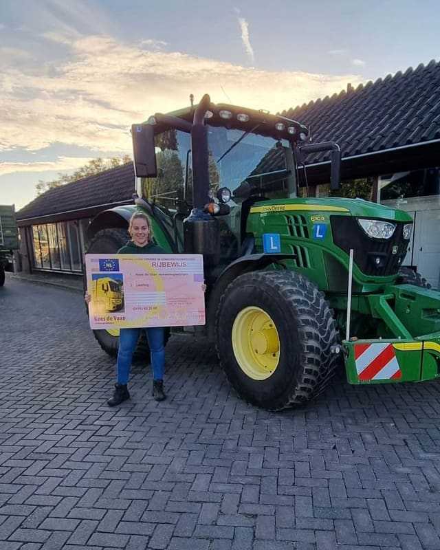 Geslaagde cursist met rijbewijsbord naast een groene lestrekker bij zonsondergang