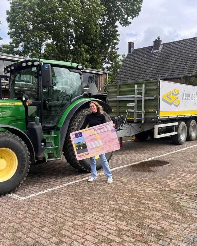 Geslaagd voor het T-rijbewijs: cursist met rijbewijsbord tussen lestrekker en aanhangwagen