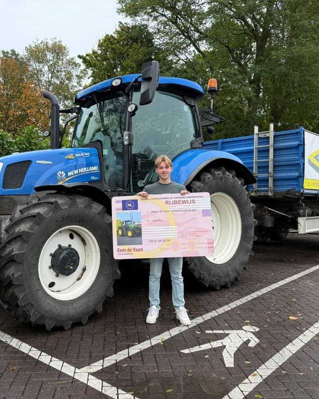 Geslaagde cursist met rijbewijsbord voor een blauwe lestrekker met blauwe kipper