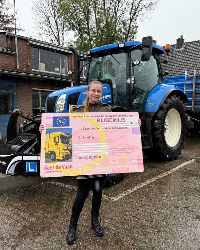 Geslaagd voor het trekkerrijbewijs: cursist met rijbewijsbord voor een blauwe lestrekker met L-bord