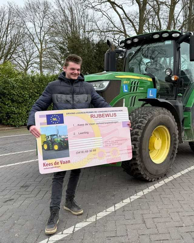 Geslaagde cursist in donkere jas met rijbewijsbord bij een groene lestrekker