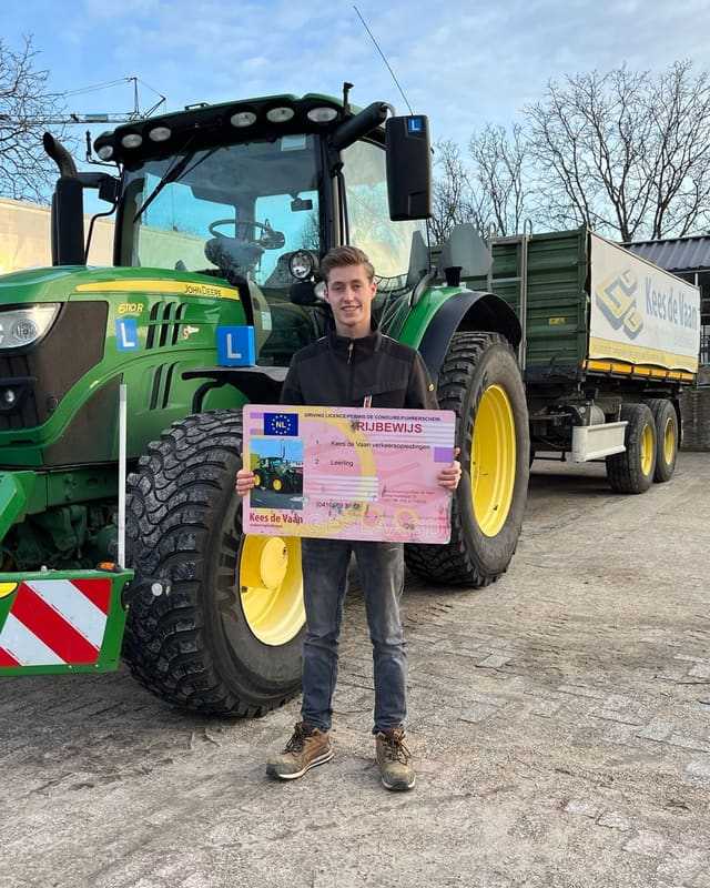 Geslaagd voor het trekkerrijbewijs: cursist met rijbewijsbord voor een groene lestrekker met L-bord en kipper