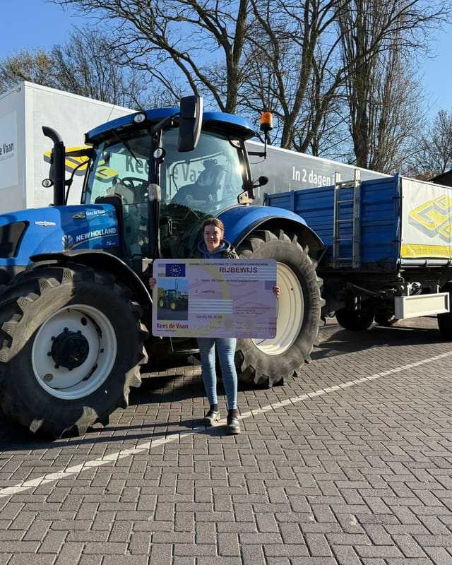Geslaagde cursist met rijbewijsbord naast een blauwe lestrekker met kipper