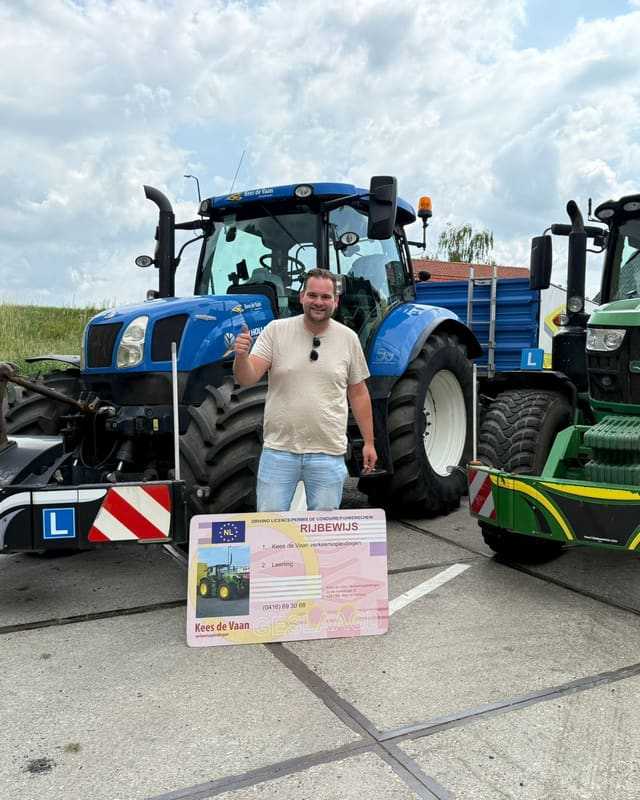 Geslaagd voor het trekkerrijbewijs: cursist in beige shirt met rijbewijsbord voor een blauwe lestrekker